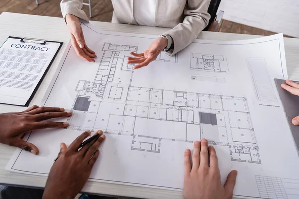 Partial view of interpreter pointing with hands at blueprint near interracial business partners — Stock Photo