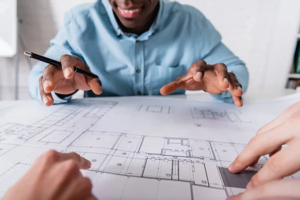 Cropped view of african american businessman gesturing near blueprint and business partners on blurred foreground — Stock Photo