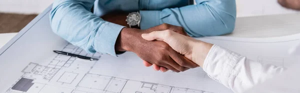 Vue partielle de l'homme d'affaires afro-américain serrant la main d'un partenaire d'affaires près du plan directeur, avant-plan flou, bannière — Photo de stock