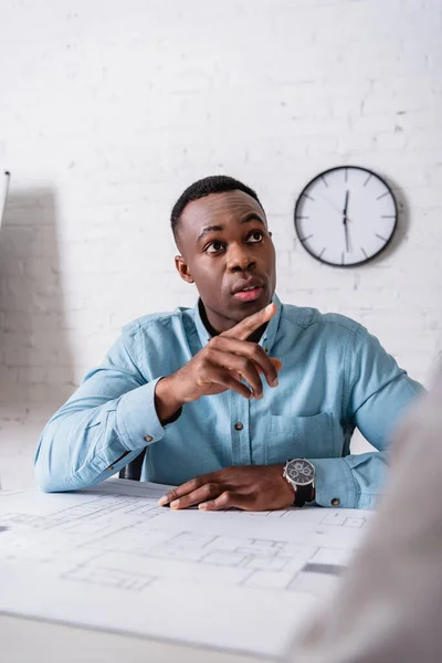 Ernsthafter afrikanisch-amerikanischer Geschäftsmann, der mit dem Finger in der Nähe der Blaupause zeigt, verschwommener Vordergrund — Stockfoto