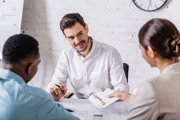 Rückseite einer Geschäftsfrau, die Bestechungsgeld an Bisinessman in der Nähe von Blaupause und afrikanisch-amerikanischem Partner gibt, unscharfer Vordergrund — Stockfoto