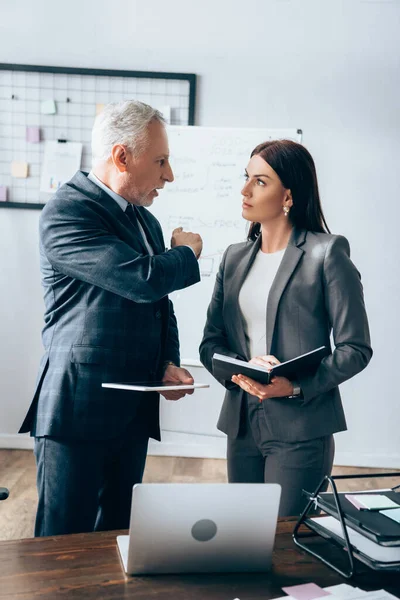 Mature advisor with digital tablet talking with businesswoman holding notebook — Stock Photo