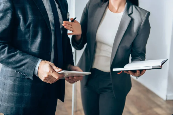 Vue recadrée de femme d'affaires avec ordinateur portable et stylo pointant vers l'investisseur avec tablette numérique — Photo de stock