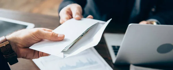 Ausgeschnittene Ansicht des Geschäftsmannes, der Umschlag mit Geld von einem Investor in der Nähe von Laptop auf verschwommenem Hintergrund nimmt, Banner — Stockfoto