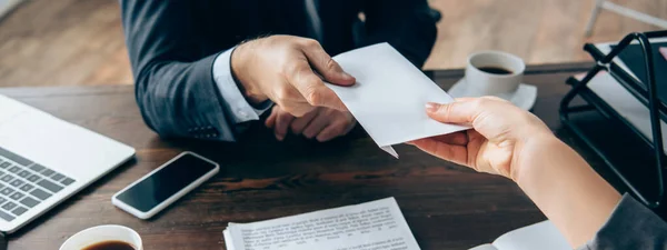 Vista recortada de la mujer de negocios tomando sobre de inversionista cerca de café y dispositivos en la mesa, pancarta - foto de stock