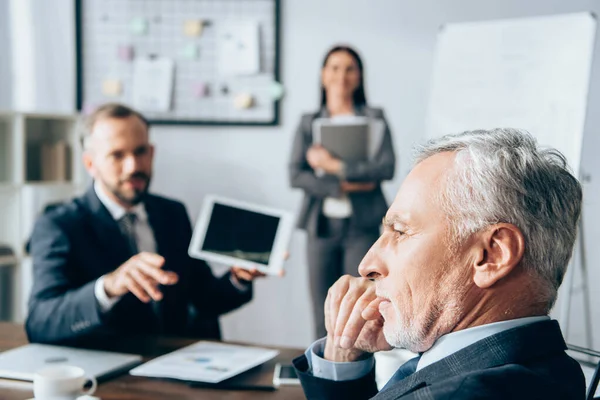 Pensive investor sitting near business people on blurred background in office — Stock Photo