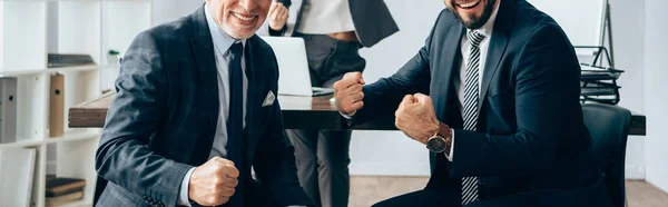 Cropped view of smiling businessman showing yeah gesture near businesswoman on blurred background in office, banner — Stock Photo