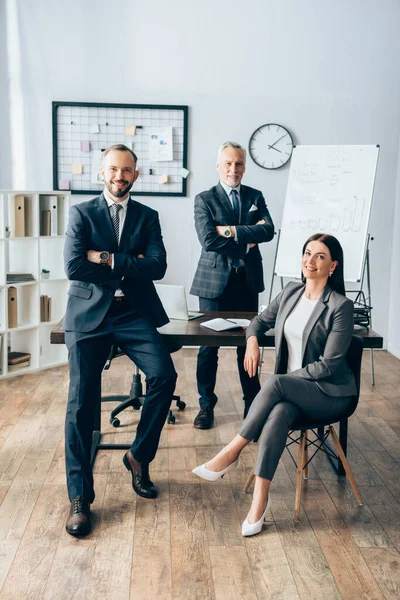 Smiling businesswoman sitting near partners in office — Stock Photo