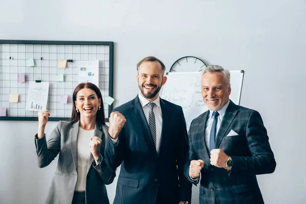 Cheerful businesspeople showing yeah gesture near flipchart in office — Stock Photo