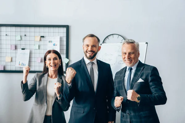 Uomini d'affari allegri che mostrano sì gesto vicino flipchart in ufficio — Foto stock