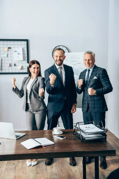 Positive Geschäftsleute mit Ja-Geste in der Nähe von Geräten und Flipcharts im Büro — Stockfoto