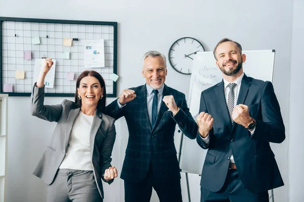 Smiling business people showing yeah gesture at camera near flipchart in office — Stock Photo