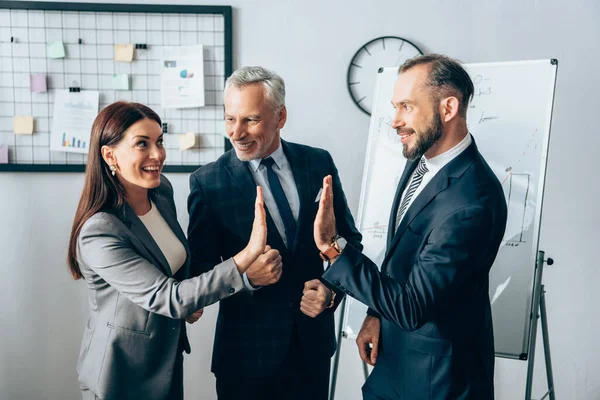 Smiling businesspeople giving high five near mature colleague in office — Stock Photo