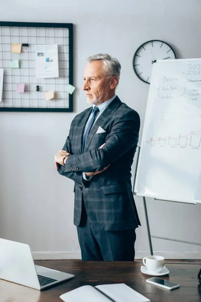 Зрелый бизнесмен, стоящий рядом с устройствами и кубком в офисе — стоковое фото