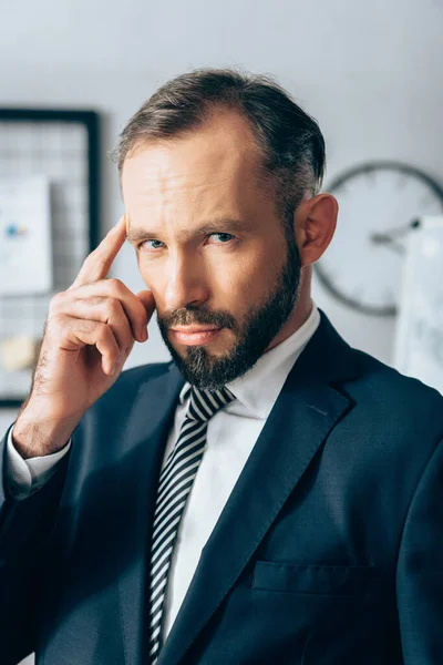 Businessman in formal wear looking at camera and pointing with finger at head in office — Stock Photo