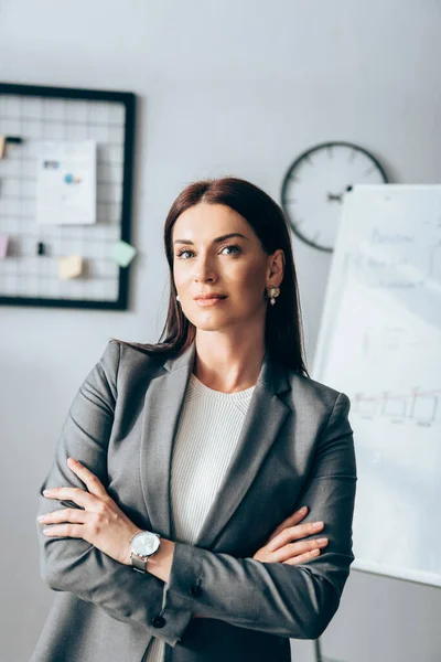 Geschäftsfrau mit verschränkten Armen blickt im Büro in die Kamera — Stockfoto