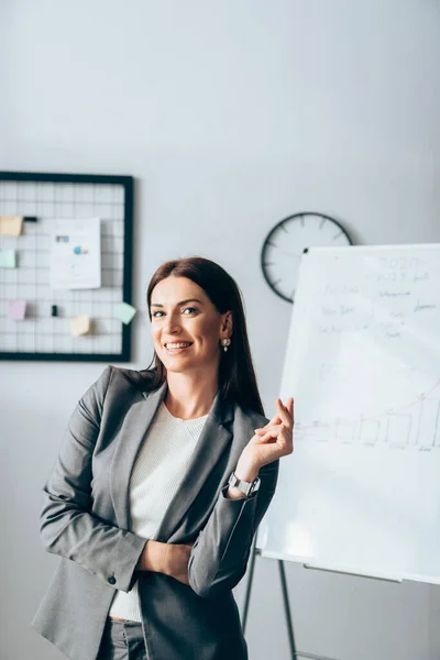 Femme d'affaires souriante regardant la caméra près de tableau à feuilles mobiles sur fond flou — Photo de stock