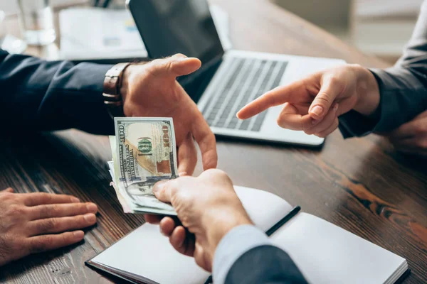 Vista recortada de la mujer de negocios apuntando al dinero cerca de los hombres de negocios en primer plano borroso - foto de stock