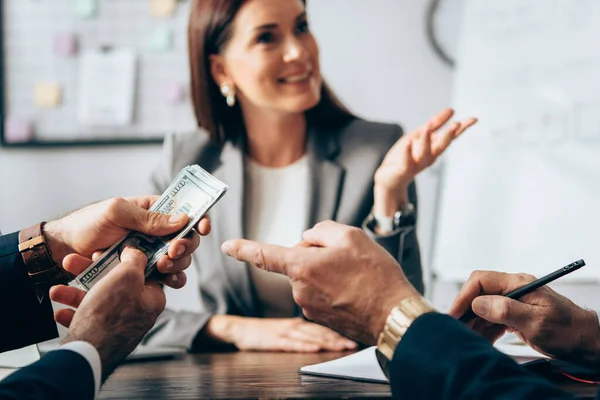 Businessman pointing at dollars near colleague and businesswoman on blurred background — Stock Photo