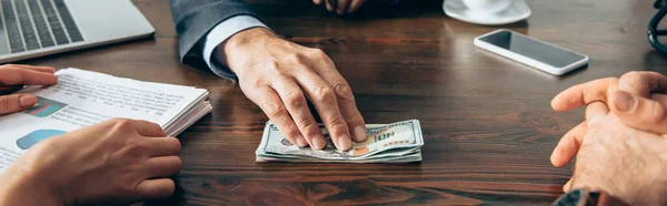 Cropped view of businessman holding dollars near partners with papers on blurred foreground, banner — Stock Photo