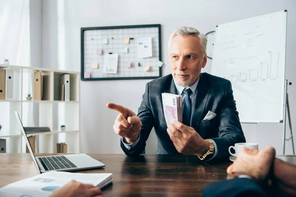 Investor mit Geld zeigt auf Geschäftsfrau mit Dokumenten im verschwommenen Vordergrund — Stockfoto