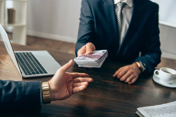 Cropped view of businessman taking money from investor near laptop and papers on blurred background — Stock Photo