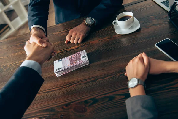 Cropped view of investor and businessman handshaking near euro banknotes and businesswoman on blurred foreground — Stock Photo