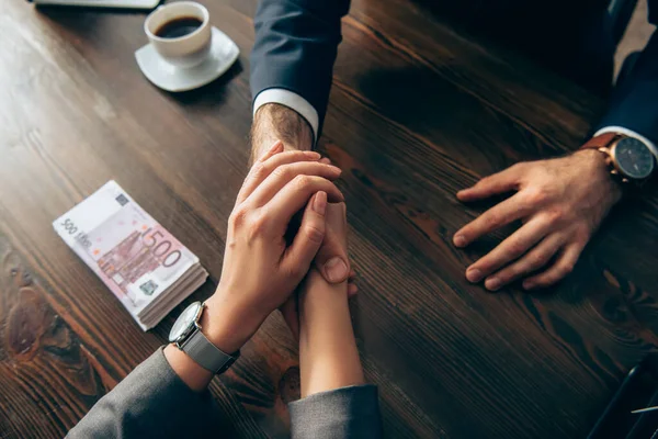 Cropped view of business people shaking hands near euro banknotes and coffee on blurred background — Stock Photo