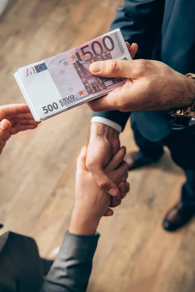 Ausgeschnittene Ansicht von Anlegern, die Euro-Banknoten geben, und Händeschütteln mit Geschäftsfrau auf verschwommenem Hintergrund — Stockfoto