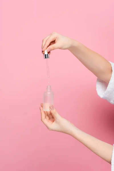 Cropped view of young woman in bathrobe holding serum on pink — Stock Photo