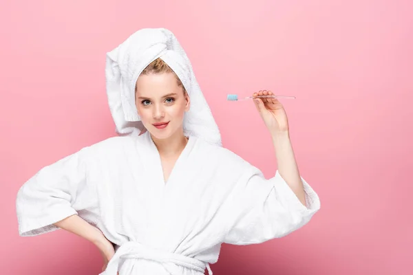 Young woman in bathrobe with towel on head holding toothbrush on pink — Stock Photo