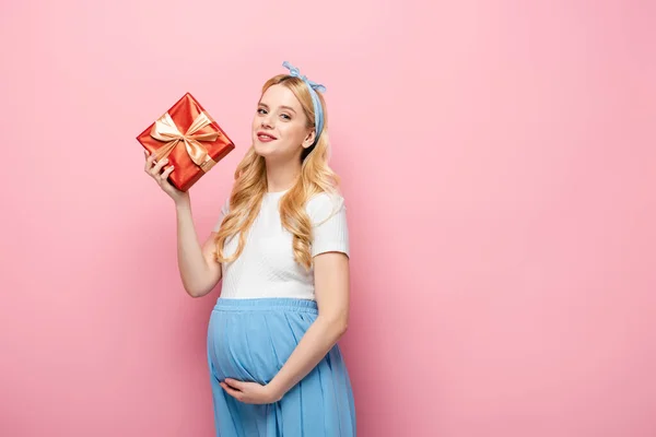 Блондинка беременная женщина с подарочной коробкой на розовом фоне — стоковое фото
