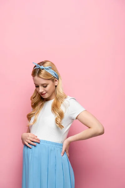Blonde young pregnant woman looking at belly on pink background — Stock Photo