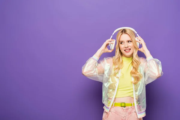 Sorridente bionda giovane donna in abito colorato e cuffie su sfondo viola — Foto stock