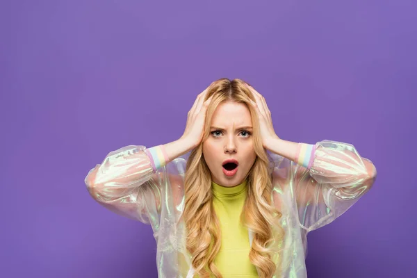 Choqué jeune femme blonde en tenue colorée tenant la tête sur fond violet — Photo de stock
