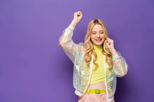 Glücklich blonde junge Frau in buntem Outfit zeigt yeah Geste auf lila Hintergrund — Stockfoto