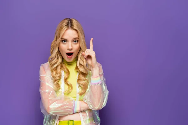 Erstaunt blonde junge Frau in buntem Outfit zeigt Idee Geste auf lila Hintergrund — Stockfoto