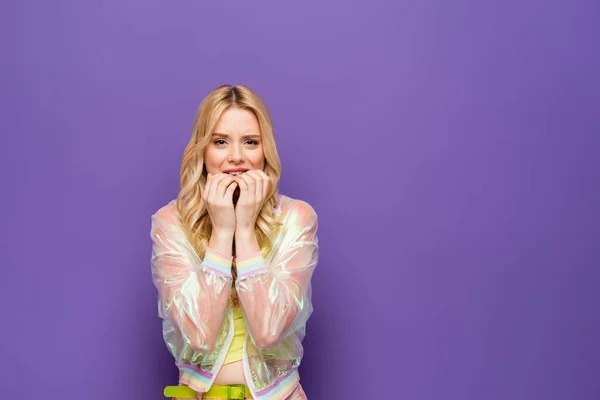 Scared blonde young woman in colorful outfit on purple background — Stock Photo