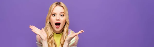 Shocked blonde young woman in colorful outfit isolated on purple, banner — Stock Photo