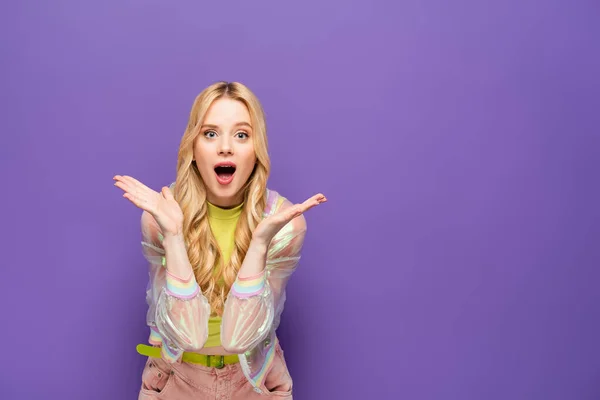 Choqué jeune femme blonde en tenue colorée sur fond violet — Photo de stock