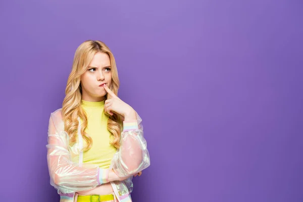 Pensive blonde young woman in colorful outfit on purple background — Stock Photo