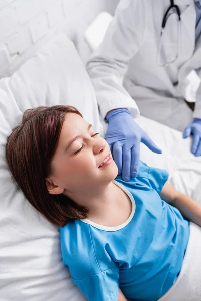 Лікар торкається дитини, лежачи в лікарняному ліжку з закритими очима, розмитий фон — стокове фото