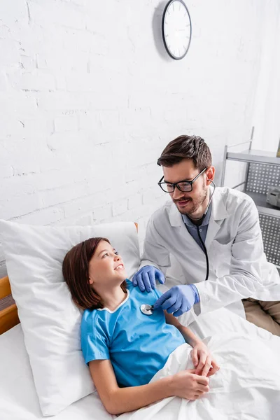 Lächelnder Kinderarzt untersucht fröhliches Mädchen mit Stethoskop im Krankenhaus — Stockfoto