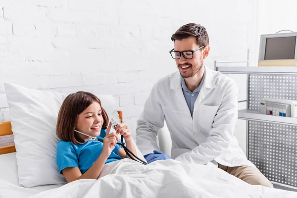 Happy child holding stethoscope near smiling pediatrician — Stock Photo