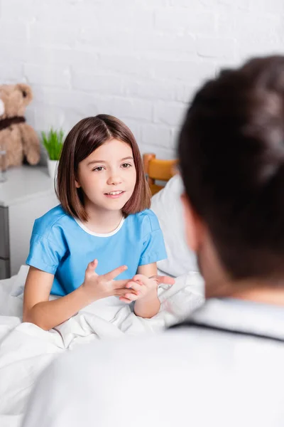 Lächelndes Mädchen gestikuliert im Gespräch mit Arzt auf verschwommenem Vordergrund — Stockfoto