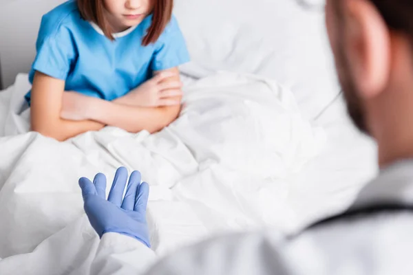 Menina triste com braços cruzados perto médico gesticulando em primeiro plano desfocado — Fotografia de Stock