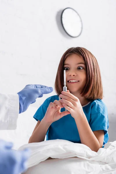 Chica asombrada sosteniendo la jeringa cerca del médico en primer plano borrosa - foto de stock