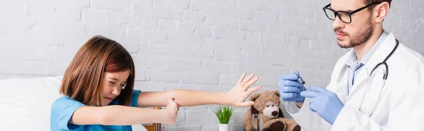 Frightened girl showing refuse gesture near doctor with syringe, banner — Stock Photo