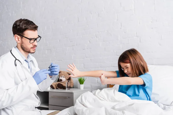 Scared girl with closed eyes showing stop gesture near doctor with syringe — Stock Photo