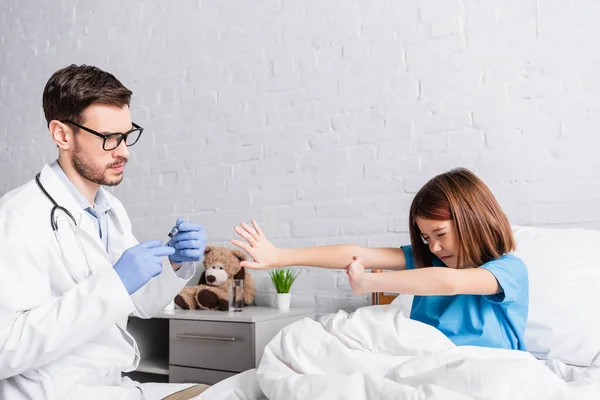 Chica asustada con los ojos cerrados mostrando gesto de stop cerca del médico con jeringa - foto de stock